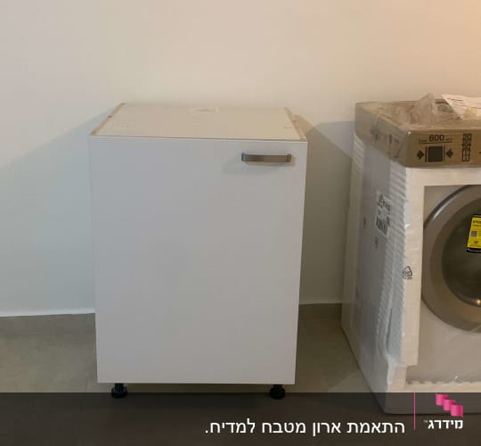 ארון מטבח לבן ליד מכונת כביסה באריזה